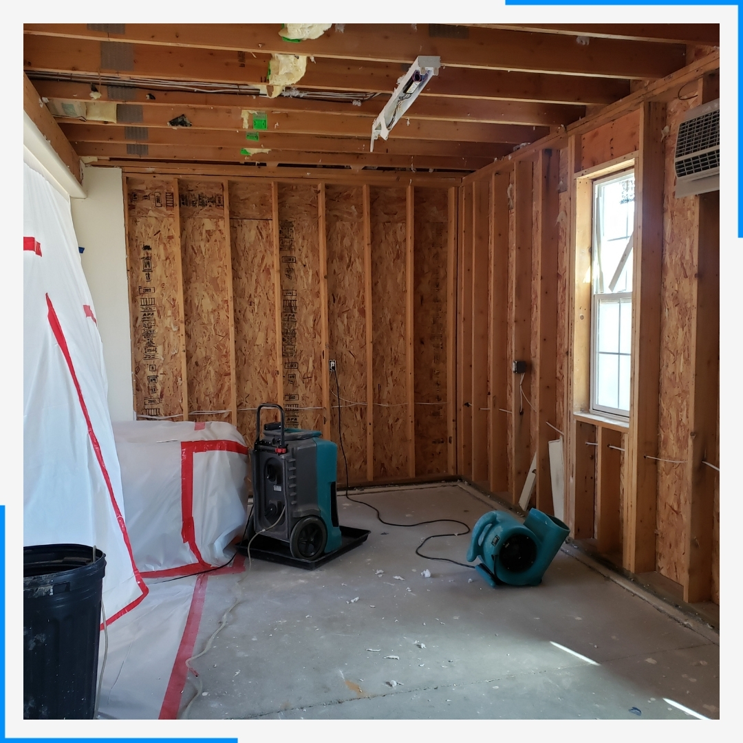 A room undergoing water damage restoration, with exposed wood framing and industrial drying equipment on the floor.