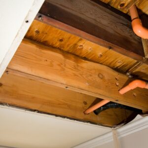 The view from below of water-soaked wooden ceiling joists and pipes, showing hidden structural water damage.