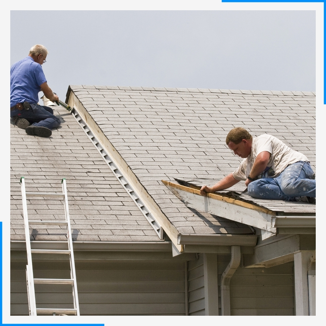 Two roofers are on top of a house repairing damaged shingles, with a ladder leaning against the side.