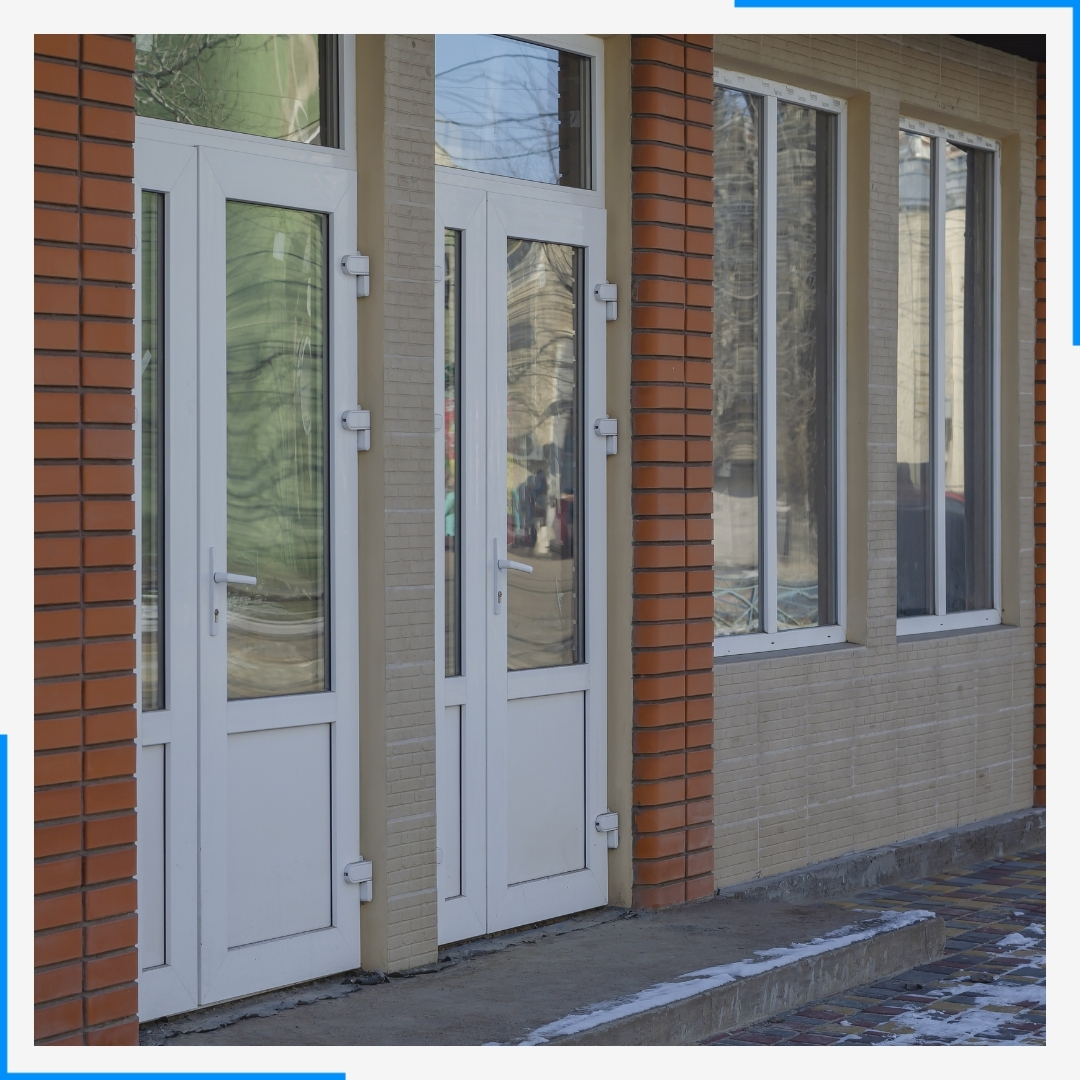 The entrance of a building with white-framed glass doors set between columns of red brick.