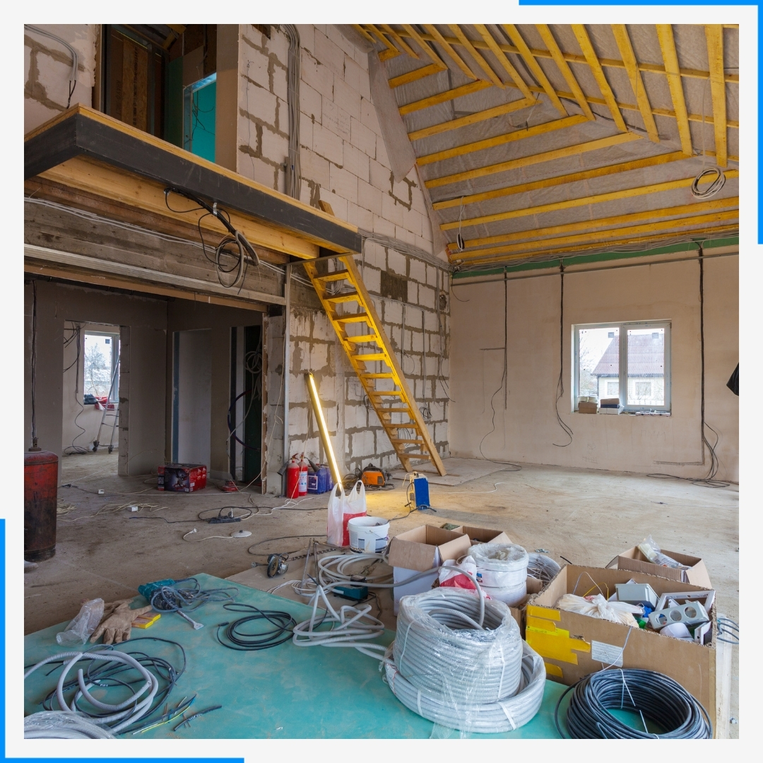 The interior of a building during construction, showing exposed block walls, wood ceiling joists, and various tools and materials.